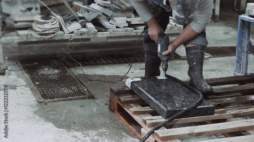 The employee makes the holes in the marble stone plate