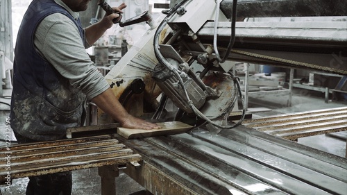 Worker uses saw machine for cutting marble stone piece