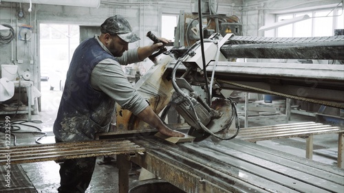 Worker uses saw machine for cutting marble stone piece