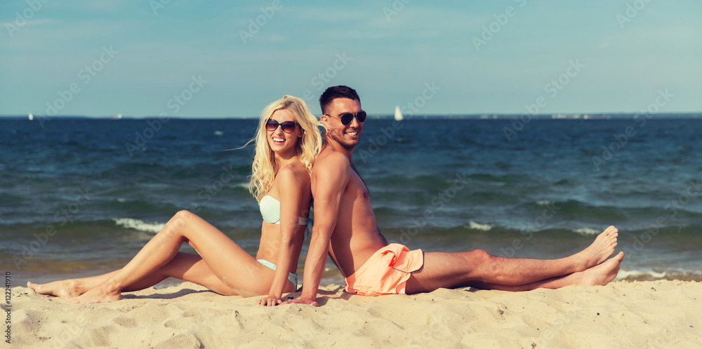 happy couple in swimwear sitting on summer beach