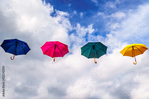 Blue Umbrella, Red Umbrella, Green Umbrella and Yellow Umbrella floating in the Air under blue sky and clouds