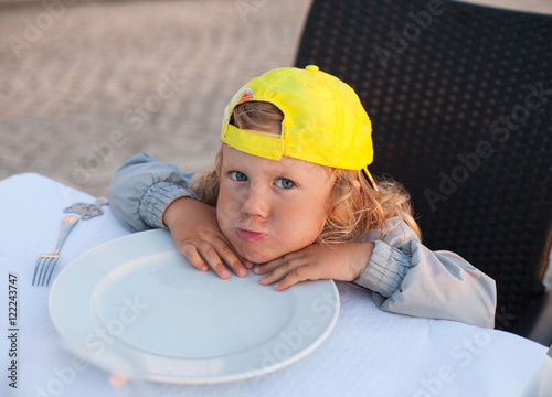 Little kid with curly hair waiting meal at outdoor restaurant
