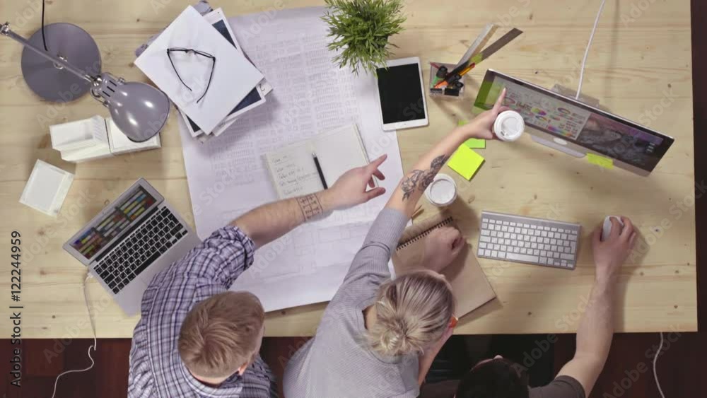 Top view of three designers working in team on house project. They choosing and discussing colors at the computer screen
