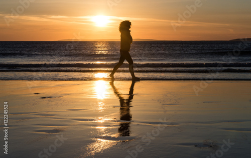 silhouette of woman walking on the beach at sunset © Gabriel Cassan