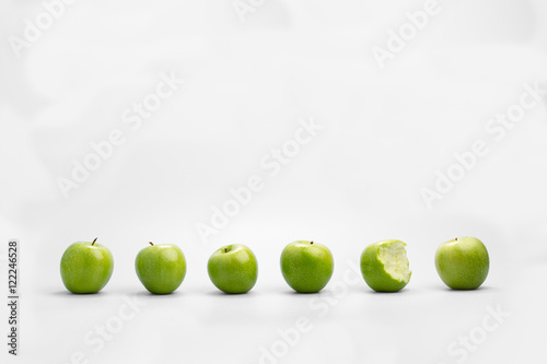 Принти на полотні Row of whole green apples with one eaten