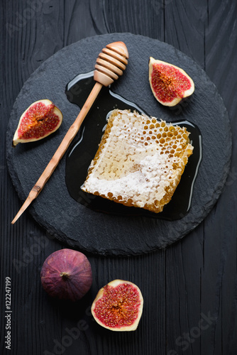 Fresh honey with ripe figs over black wooden surface, above view