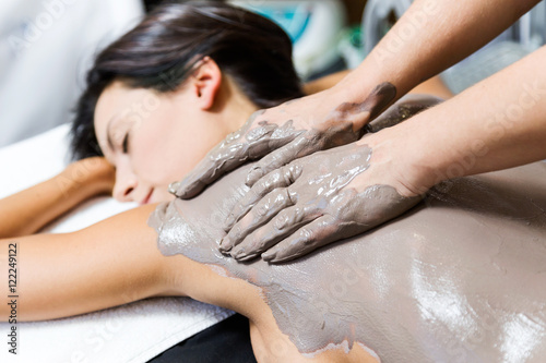 Beautiful young woman having clay body mask apply by beautician. photo