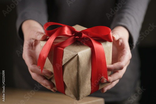 female teen girl shows paper gift box with red ribbon and a bow