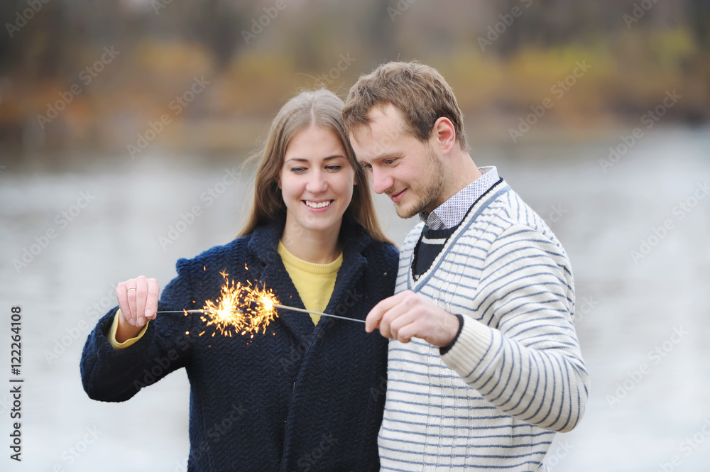The young happy couple holding a bengal light on the river bank.