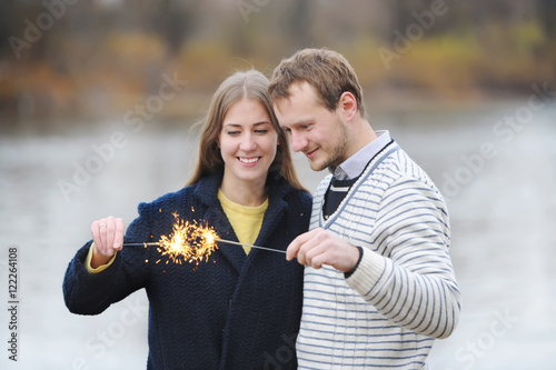 Obraz na płótnie The young happy couple holding a bengal light on the river bank. w salonie