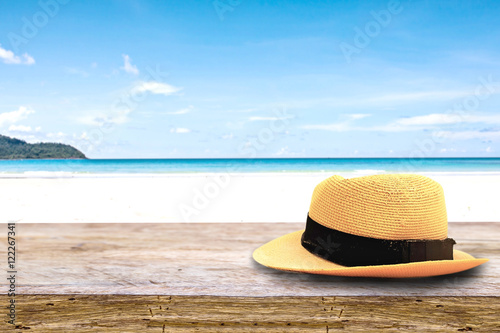 Fototapeta Naklejka Na Ścianę i Meble -  hat on on wood terrace over blue sea and tropical island beach background. Image for Summer Holiday Vacation concept.
