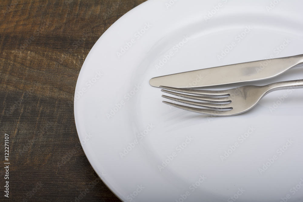 Empty white dish with spoon and fork on wood table Empty white dish with spoon and fork on wood table