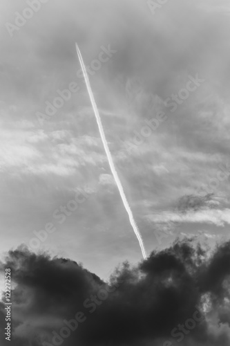 Airplane with Contrail in cloudy sky in black and white