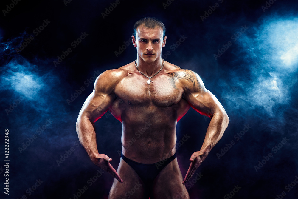 Close up on perfect abs. Strong bodybuilder with six pack.Strong bodybuilder man with perfect abs, shoulders,biceps, triceps and chest, personal fitness trainer flexing his muscles in blue, red smoke
