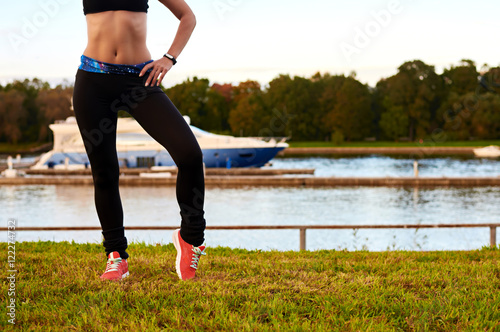 Athletic body and legs of sport girl in the park near river. Cpy space for advertising. Girl in fitness dark wear training legs before or after run.