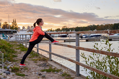 Adult person in sport wear stretch legs in evening training after running. Sport outdoor fitness concept for advertising with copy space for a text.