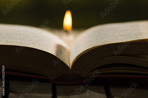 Thick book lying open on wooden surface, wax candle sitting next to it, beautiful night light setting, magic concept shoot