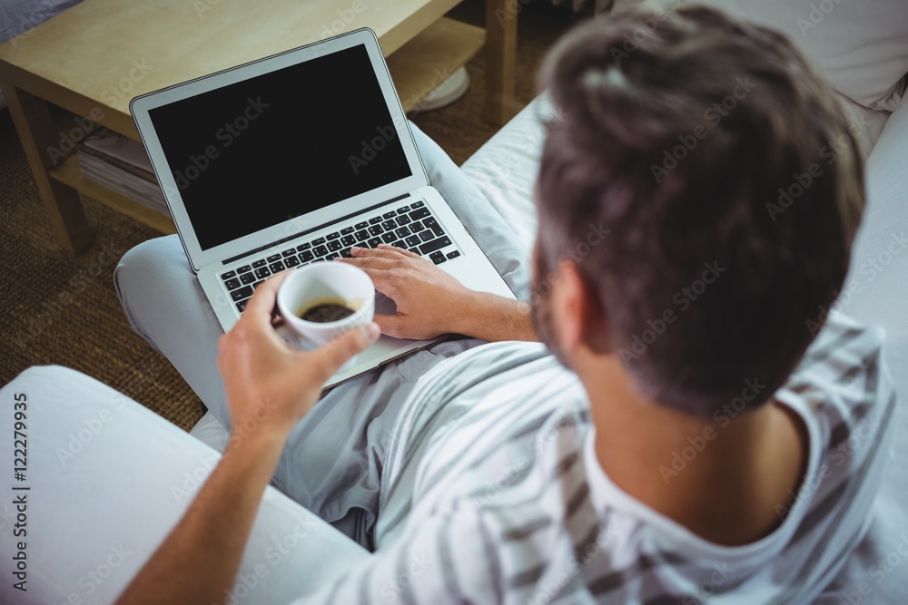 Father using laptop while having coffee in living room