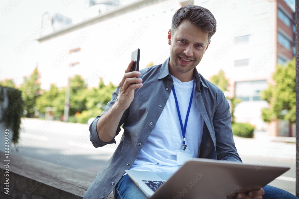 Fototapeta premium Handsome business executive holding mobile phone and laptop