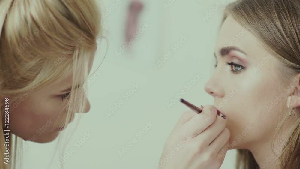Makeup artist paints lips of a beautiful girl. Model with lipstick. Maroon lipstick. Lipstick wine-colored on model s lips. Make-up artist using lipstick brush. Trendy shades of lipstick Makeup artist paints lips of a beautiful girl. Model with lipstick. Maroon lipstick. Lipstick wine-colored on model s lips. Make-up artist using lipstick brush. Trendy shades of lipstick