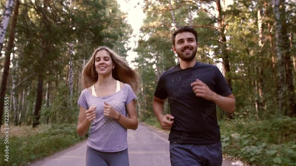 Portrait of cheerful blond woman and handsome man jogging in the forest together Portrait of cheerful blond woman and handsome man jogging in the forest together