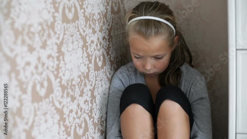 Little aggrieved girl sitting in the corner of a room with a sad face