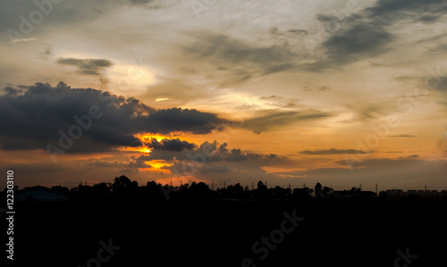 weather scene at sunset with silhouettes of houses against a bur © saelim