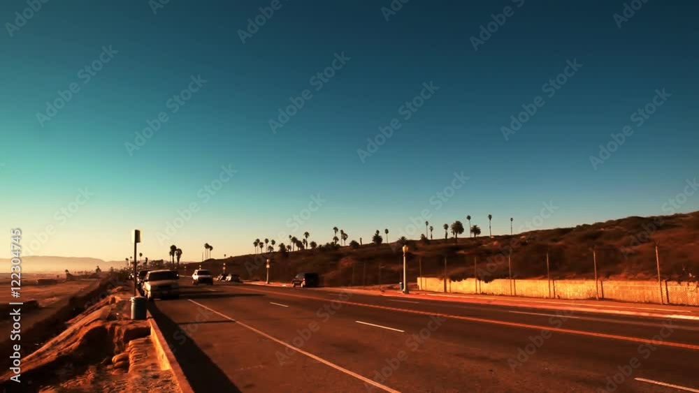 A stationary shot of afternoon traffic driving along the California coast.