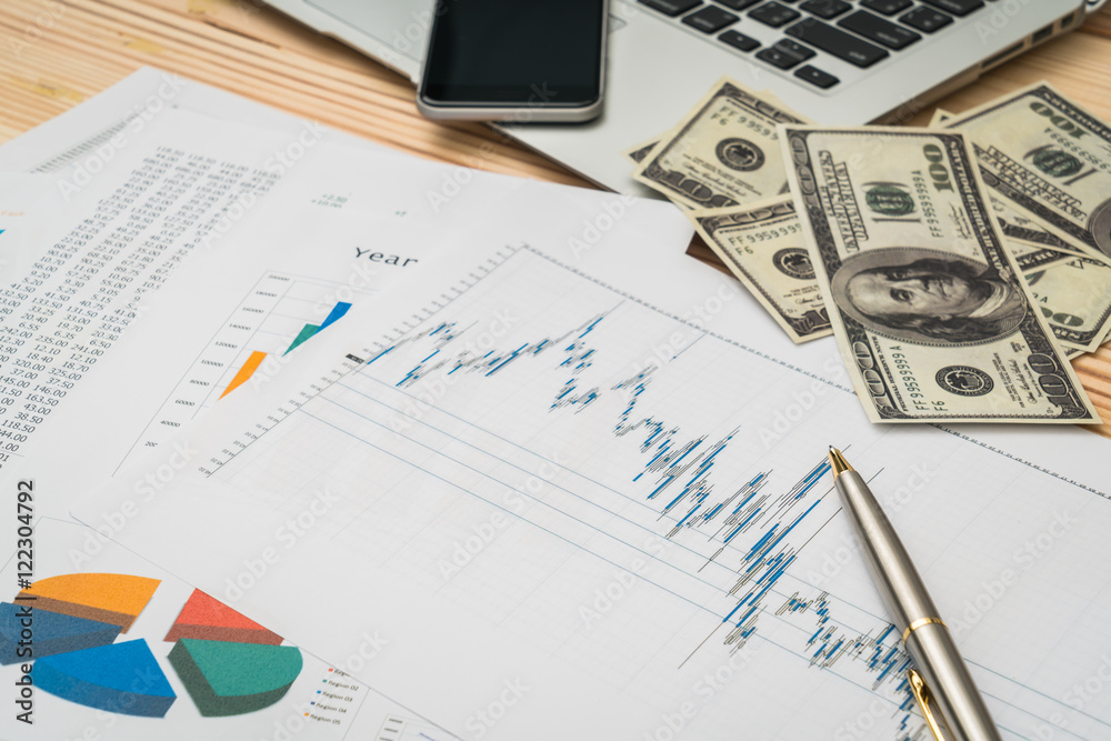 Financial charts on the table with laptop , phone ,dollars bankn Financial charts on the table with laptop , phone ,dollars bankn