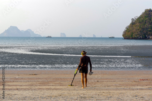 Treasure hunter with Metal detector on sunrise the beach