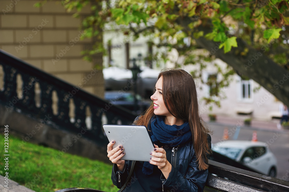 Young girl sitting on a bench , communication through the Internet , in the hands of the tablet. Young girl sitting on a bench , communication through the Internet , in the hands of the tablet.