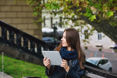 Young girl sitting on a bench , communication through the Internet , in the hands of the tablet.