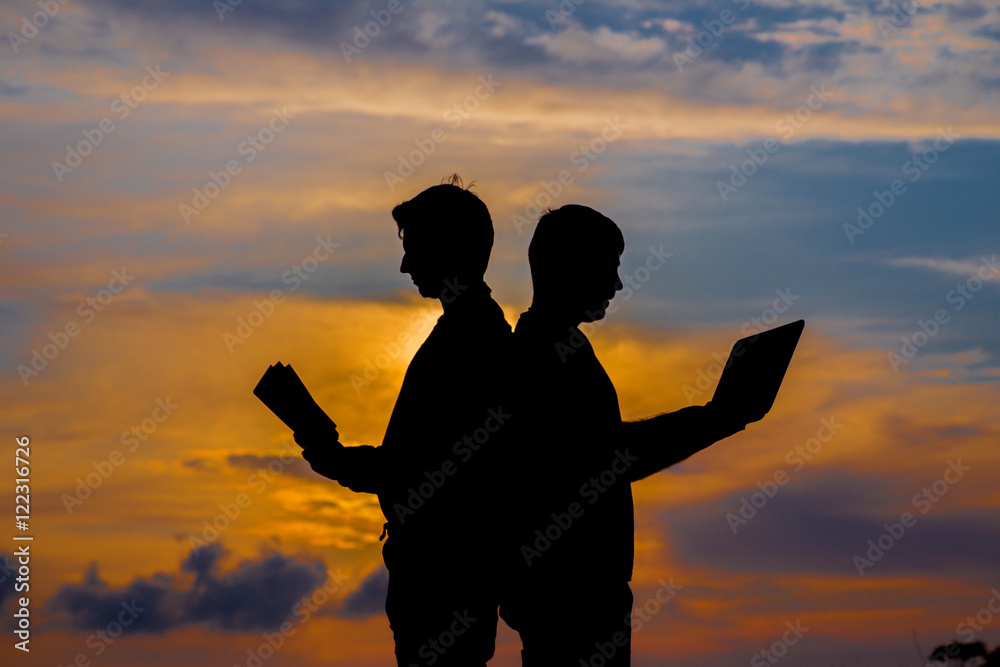 silhouette of a men with laptop and a book on sunset or sunrise