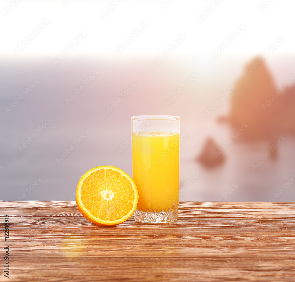 Naklejka premium Tall glass of tasty freshly squeezed orange juice standing on an outdoor wooden picnic table on a hot summer day