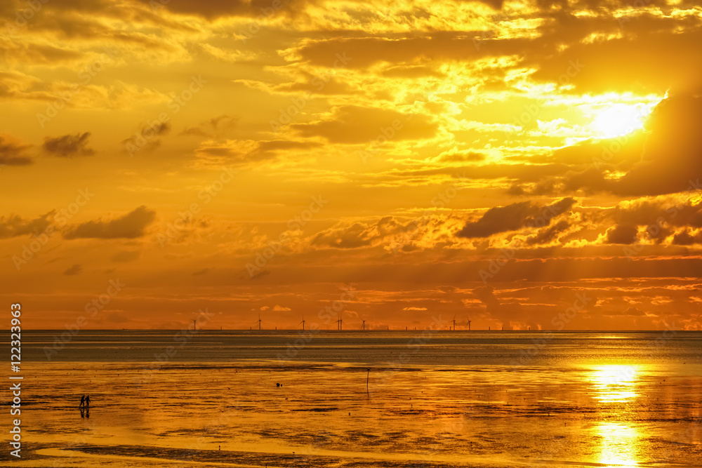 Ein Pärchen spaziert im Sonnenuntergang durch das Wattenmeer mit einem Offshore Windpark am Horizont Ein Pärchen spaziert im Sonnenuntergang durch das Wattenmeer mit einem Offshore Windpark am Horizont