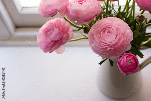High angle close up of pink ranunculus in white jug on window sill (selective focus)
