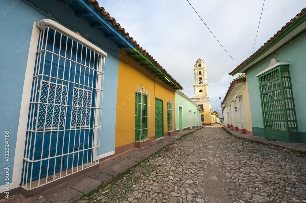 Scenic view of traditional colonial architecture with the bell tower of the church of San Francisco de Asis at the end of the cobble street in Trinidad, Cuba