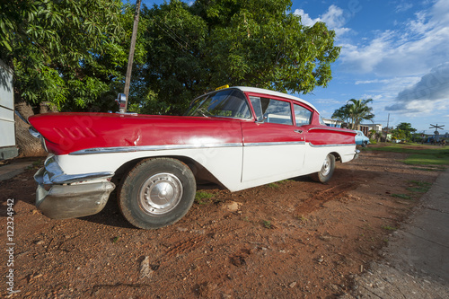 Vintage American car sits parked on a brown dirt driveway on the outskirts of Trinidad  Cuba