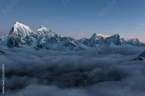 Mountain Cholatse view from Gokyo Ri. Beautiful mountain valley covered with grey gloomy clouds at sunset. Dramatic snowy peak rising above field of clouds. Himalayas, Nepal. photo