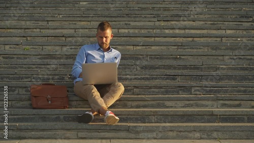 Attractive businessman sitting on a college campus with laptop computer. Education technology lifestyle.