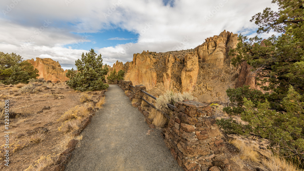 Colorful Canyon. Amazing landscape of yellow sharp cliffs. Pathway with guard among the dry grass, shrubs and pine trees. Smith Rock state park, Oregon