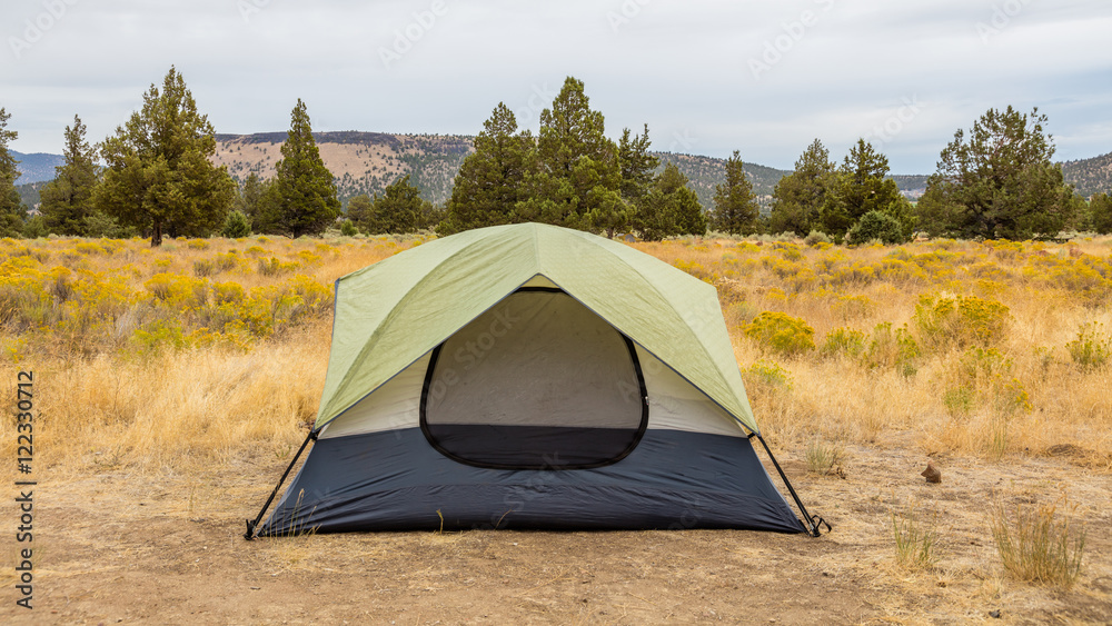 Blue-gray tent on a background of dry grass, woods and hills. Dry yellow grass grows on the slopes of the mountains. Beautiful landscape of trees and hills. Smith Rock state park, Oregon