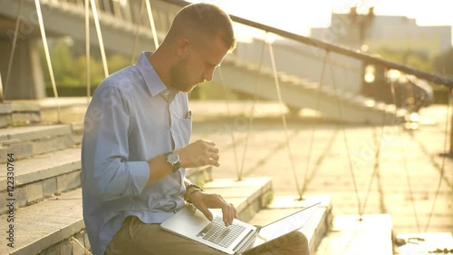 Happy student browsing the internet on his laptop and sitting outdoor