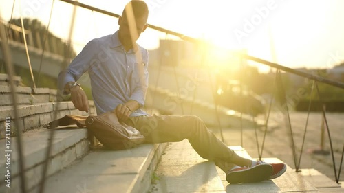 hipster businessman with laptop sits on the stairs and works at sunset