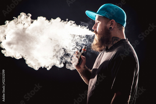 Men with beard  in sunglasses vaping and releases a cloud of vapor.