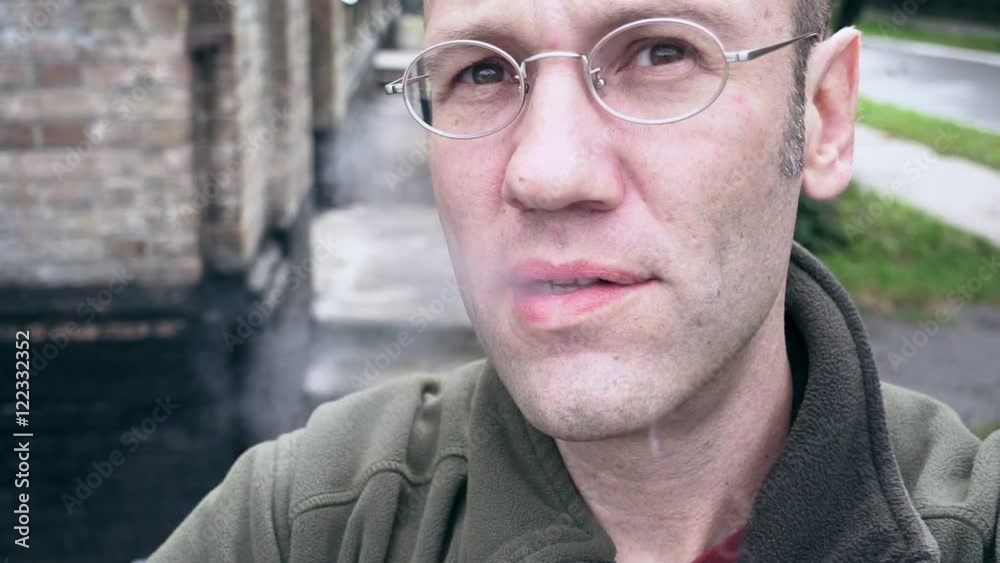 A man is exhaling the smoke cloud from his mouth in slow motion. E-cigarettes are the new sensation of smoking culture. Vapor does not need flame to start it. A man is exhaling the smoke cloud from his mouth in slow motion. E-cigarettes are the new sensation of smoking culture. Vapor does not need flame to start it.