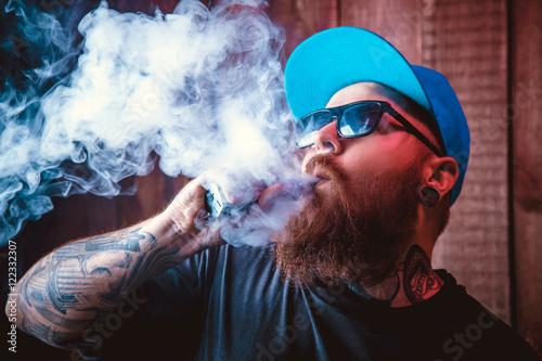 Men with beard  in sunglasses vaping and releases a cloud of vapor.