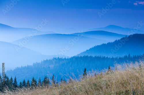 Landscape of misty mountain hills covered by forest.