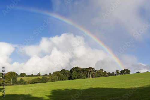 Rainbow in the fields in the early morning sunlight with blue sky and clouds, Cornwall, UK