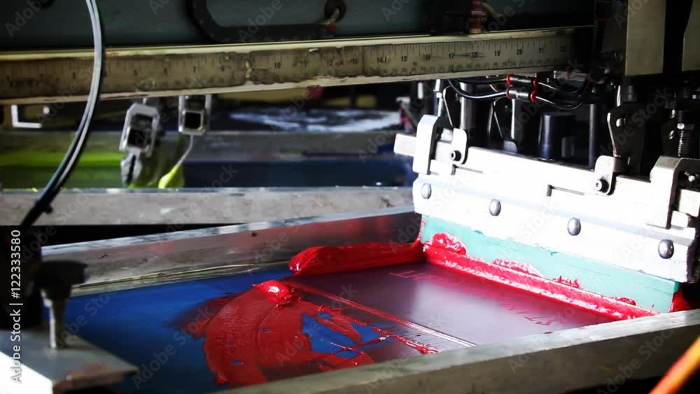 A pneumatic silk screening printing press operates.